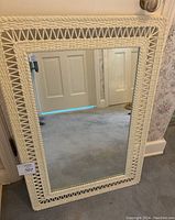 Full front view of the vintage rectangular mirror showing the cream-white plastic wicker patterned frame and reflection of a door.
