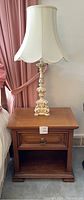 Wooden nightstand with drawer and ornate table lamp with scalloped lampshade on top