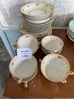 Stack of 8 plates and 8 cream soup bowls with saucers arranged on table, showing floral and gold trim details.