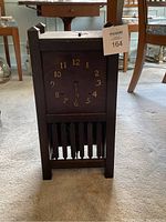Front view showing the entire clock structure with dark wooden case, carved posts, and vertical slat base.