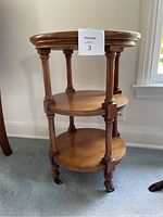 Side view of 3 tier wooden side table on wheels, showing turned legs, circular shelves and casters.