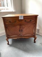Front view of the wooden side table showing drawer with brass handles and woven rattan style cabinet doors below.