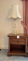 Photo of wooden nightstand with one drawer and decorative table lamp placed on top, showing front view and details
