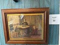 Framed wall art of mother and children at dining table, showing warm tones and wooden frame.