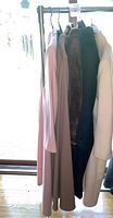 Full view of four women's coats hanging on a rack including a pink, beige, brown faux fur, and black coat.