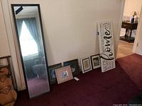 Photo showing six items including a large black framed floor mirror with corner damage, five framed artworks including a canvas print with 'home' text and four smaller framed pieces in various frames and sizes.