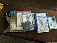 Six coffee table books arranged side by side on a brown surface showing covers and titles on nature, cats, desserts, and art.