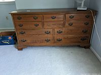 Front view of wooden Ethan Allen dresser showing 10 drawers with metal handles, scratches, and wear marks.