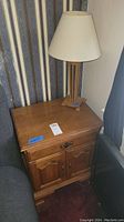 Full view of wooden end table with cabinet doors and drawer, lamp placed on top, showing scratches and wear.