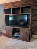 Front view of wooden entertainment center with TV placed inside central compartment. Shows shelving and cabinet doors below TV space.