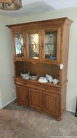 Front view of wood hutch showing decorative glass doors, open middle shelf, and lower cabinets with drawers.