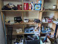 Photo of multiple shelves containing garden gloves, cleaning supplies including OxiClean, a red Coleman lantern, Schumacher charger, and assorted hand tools in containers and crates below.