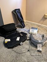 Various medical and massage devices arranged on floor including seat cushion, neck massager, leg brace, blood pressure monitor, pulse oximeter.
