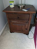 Front view of the wood look nightstand showing one drawer and lower cabinet door with round knobs, and visible surface scratches and scuffs