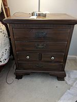 Front view of wooden four-drawer nightstand showing drawer handles, two small drawers with white knobs, dark finish, and bracket feet.
