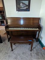 Front view of Baldwin upright piano with matching bench, showing piano keys and wood finish