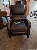 Front view of dark brown leather look recliner chair, showing worn areas especially on arms and seat cushions. Includes repair patches placed on the seat.
