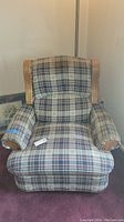 Frontal photo showing the plaid upholstered recliner with curved wooden armrests and back accents.
