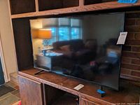 Full view of the TV sitting on wooden shelving, showing screen and remote on shelf