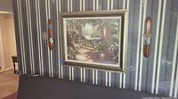 Framed garden scene wall art hanging on striped wallpaper next to one wall sconce.