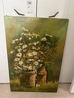 Photo of unframed floral painting on canvas showing daisies in rustic containers with green backdrop, signed Piniero.