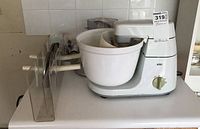Braun stand mixer with white mixing bowl, beaters attached, olive green dial, and clear plastic parts on side