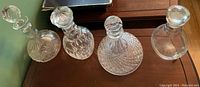 Four assorted glass decanters of various styles and shapes displayed on a wooden surface.
