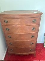 Front view of wood dresser showing five drawers with metal ring pulls and medium brown finish.