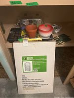 Photo of boxed JYSK Belize 3 tier greenhouse with various pots, seed trays, gloves and small garden tools on shelf above.
