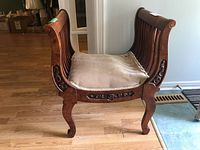 Side view of wooden horseshoe bench showing curved armrests, detailed carved accents on side, cabriole legs, and sagging upholstered seat cushion.