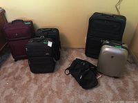 Full view of five pieces of luggage: 2 soft suitcases on wheels by Samsonite, 1 large soft suitcase by Pacific Coast, 1 silver hard shell Heys suitcase, and 1 black duffle bag.
