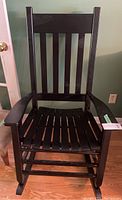 Front view of the black rocking chair showing vertical slats on back and slatted seat with armrests.