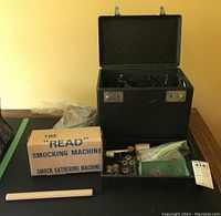 Overview of lot: hard case open showing Singer machine, The “Read” smocking machine box, accessory tray with spools and attachments, and wooden dowel