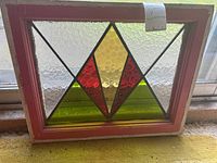 Photo of vintage stained glass window panel with geometric colored glass design in red, yellow, green, and clear textured glass framed in reddish wood
