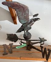 Front view of the flying eagle weather vane showing the eagle perched on a spherical brass base with directional indicators N, S, E, W and the arrow with feathered tail.