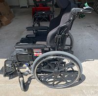 Side view of black non-folding wheelchair showing large rear wheel, armrest, side frame, and footrest.