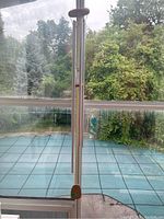 Full view of a tall metal wind chime with wooden top and clapper against a screen door with greenery outside