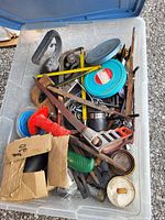 Plastic bin filled with assorted hand tools and hardware showing variety and condition of the items