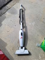 Single image showing a white Bissell stick vacuum cleaner placed on a concrete surface with power cord wrapped around the handle.