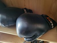 Close-up photo showing a pair of black Drag boxing gloves with Velcro wrist strap on a wood shelf.