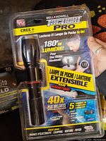 Photo of the Bell + Howell Tactical Pro flashlight in original sealed packaging showing product features and branding.