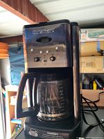 Photo of the black Cuisinart drip coffee maker with glass carafe and front control panel showing brand name and control knobs.
