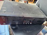 Top-front view of a Yamaha double cassette deck showing two cassette compartments, control buttons, knobs, and a headphone jack. Visible dust and wear on the surface.