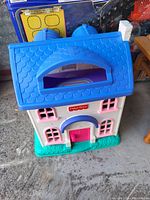 Plastic Fisher-Price kids toy house with a blue textured roof and pink door on a green base.