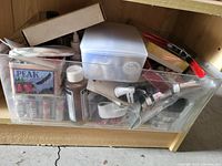 Clear plastic bin with assorted art and craft supplies inside, including paint tubes, brushes, bottles, and a box of cards.