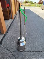 Full view of stainless steel distillation apparatus with long vertical columns, green and clear tubing, and round container base.