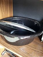 Large black oval cooking pot with glass lid shown on a wooden surface.