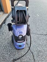 Front-facing photo of the blue Simonne pressure washer showing hose reel filled with hose and branding on the lower front panel