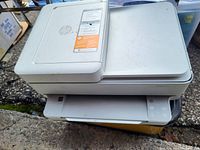 Side view of the white HP all-in-one printer showing the flatbed scanner lid and paper tray.