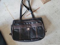 Photo of a black and brown leather purse with multiple compartments lying on floor, showing front and straps.